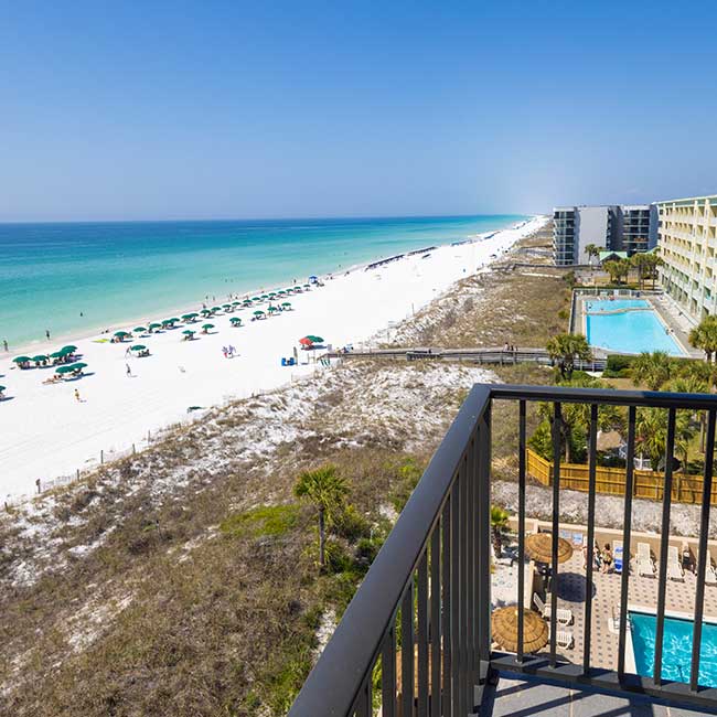 View from a balcony at Fort Walton Beach overlooking the ocean, sandy beach, and hotel pool.