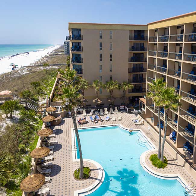 A beachfront hotel with a spacious hotel pool, palm trees, and people relaxing by the water.