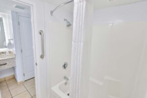 White bathroom with tub, shower, grab bar, and vanity—luxury touches fit for a penthouse hotel.