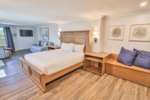 Spacious Fort Walton Beach hotel room with large bed, sofa, wall art, and wood floors.