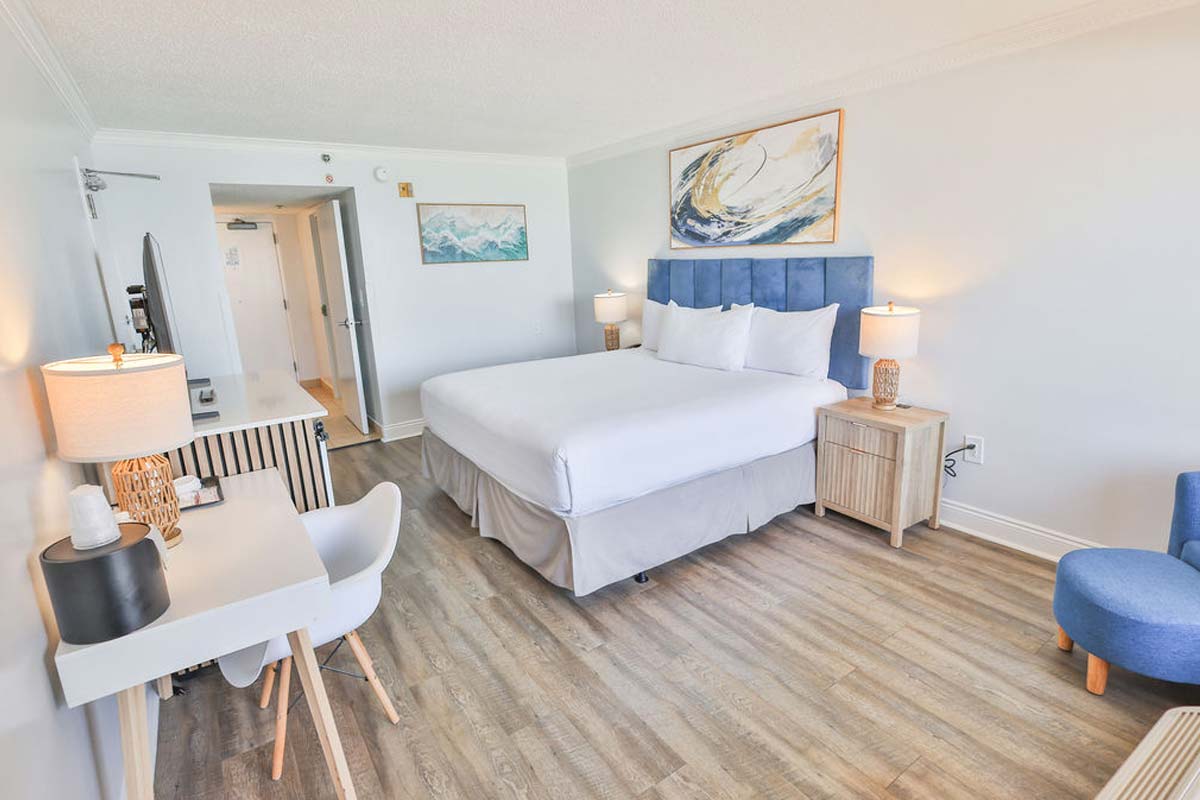 Bright penthouse hotel room with king bed, blue accents, desk, and sleek wooden floor.