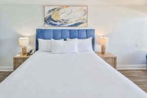 A neatly made bed with white linens, blue headboard, and abstract art in a Fort Walton Beach penthouse.