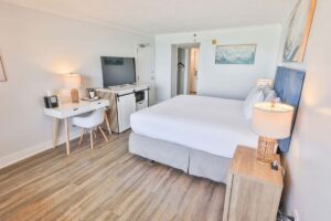 Bright hotel room with a king bed, desk, TV, wood floors, and access to the hotel pool.