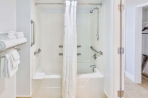 Accessible white bathtub with grab bars in a Fort Walton Beach hotel, towels on rack nearby.