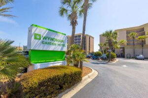 Wyndham Garden Hotel sign with palm trees, cars, hotel building, and penthouse under a clear blue sky.