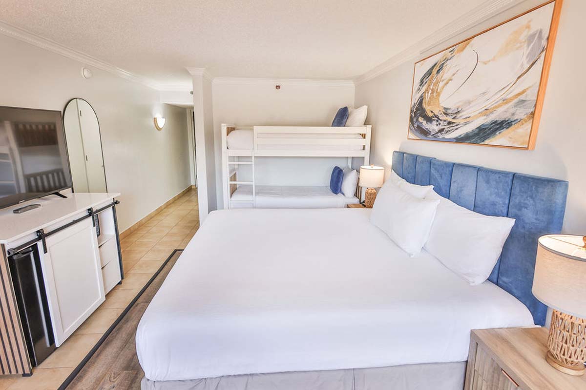Hotel room with king bed, bunk beds, TV, mini fridge—perfect for a beachfront resort stay.
