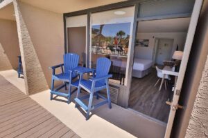 Two blue chairs on a hotel balcony, with bed and dining area visible inside.