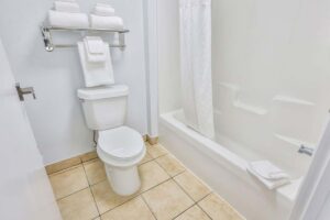 White bathroom with hotel-style tub, shower curtain, and stacked towels on towel rack.