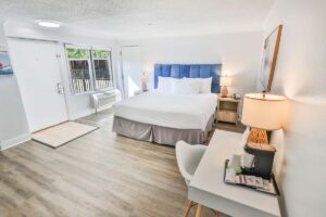 Bright penthouse hotel room with a king bed, desk, lamps, and large window with natural light.
