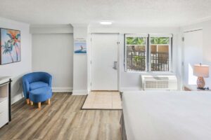Hotel room with blue chair, tropical art, wood floor, and sunlight at a Fort Walton Beach resort.