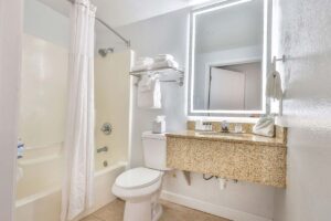 Bright hotel bathroom with a shower, toilet, granite countertop, and backlit mirror near Fort Walton Beach.