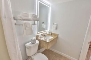 Modern bathroom in a Fort Walton Beach hotel with large mirror, sink, toilet, and white towels.