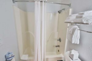 A white bathtub and shower with a curtain, towels, and shelf above a toilet in a Penthouse.