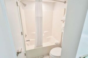 White bathroom in a Fort Walton Beach hotel, with a shower-tub combo, curtain, and fresh towels.