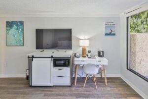 A small desk and chair beside a TV stand with a microwave in a bright Fort Walton Beach hotel room.