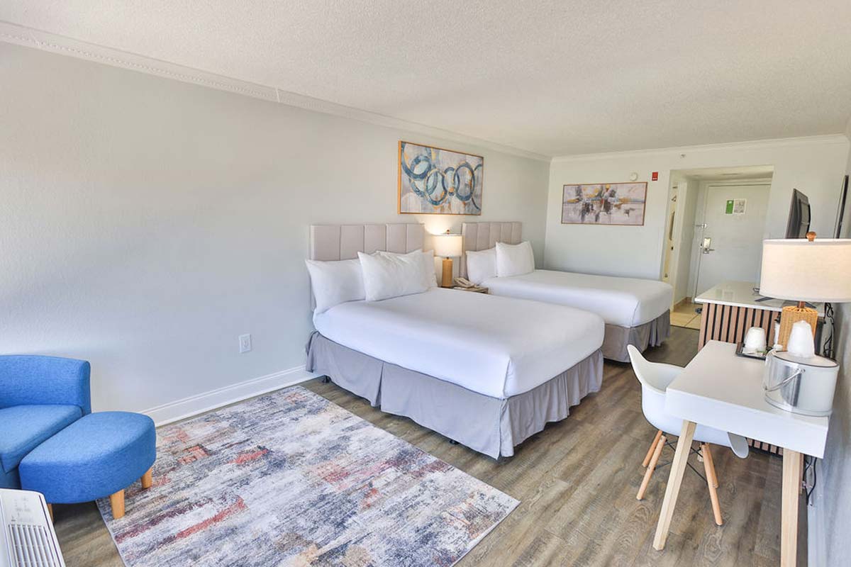 Hotel room with two beds, desk, blue chair, wall art, TV—and access to a Hotel Pool.