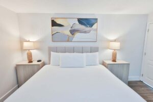 Minimalist penthouse bedroom with a neatly made bed, two lamps, and abstract art above the headboard.